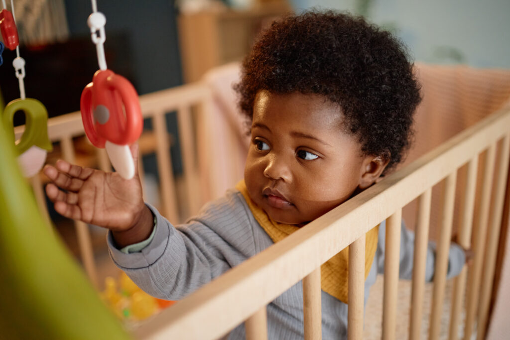 Our Curriculum awake black baby girl touching crib mobiles hanging above bed indoors